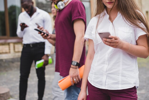 La gente de pie sosteniendo cuadernos buscando en teléfonos inteligentes