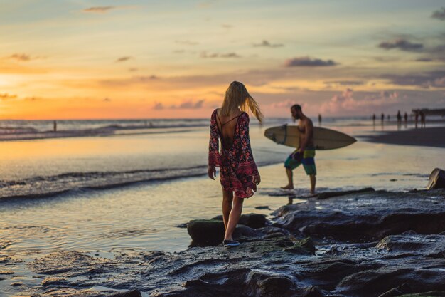 gente en la playa al atardecer. la niña está saltando contra el telón de fondo del sol poniente.