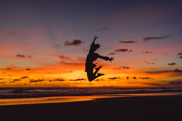 gente en la playa al atardecer. la niña está saltando contra el telón de fondo del sol poniente.