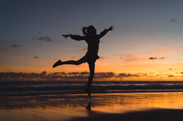 gente en la playa al atardecer. la niña está saltando contra el telón de fondo del sol poniente.