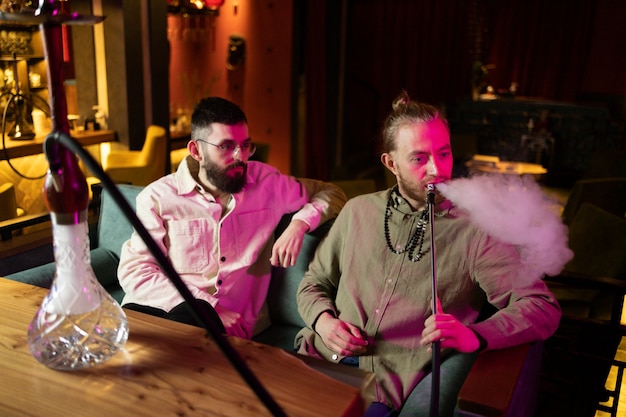 Gente relajándose vapeando desde una pipa de agua en un bar.