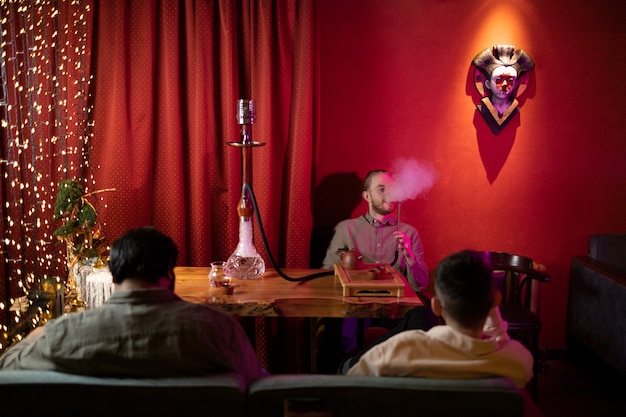 Foto gratuita gente relajándose vapeando desde una pipa de agua en un bar.