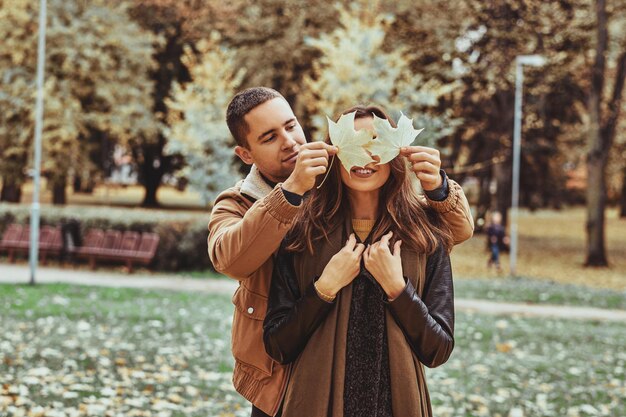 La gente romántica feliz y sonriente se divierte con la hoja de arce en el parque de otoño.
