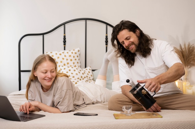 Gente sonriente con laptop y café en la cama