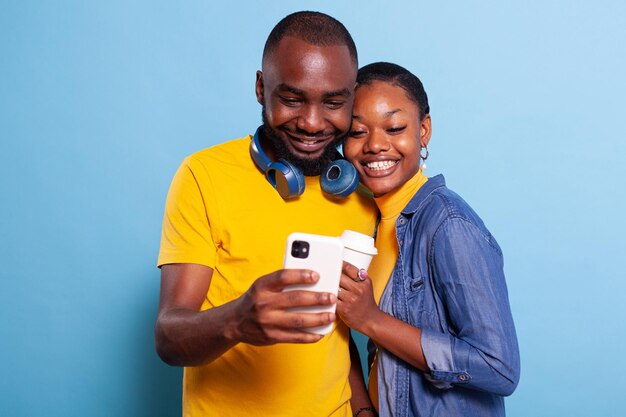 Gente sonriente tomando fotos en la cámara del teléfono inteligente, riendo y disfrutando del momento romántico. Pareja positiva haciendo recuerdos con selfies y expresando afecto el uno por el otro.