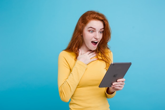 Gente y Tecnología Concepto - Close up Retrato joven hermosa atractiva redhair niña feliz sonriendo en la mesa digital con algo ganando. Fondo De Pastel Azul. Copie el espacio.