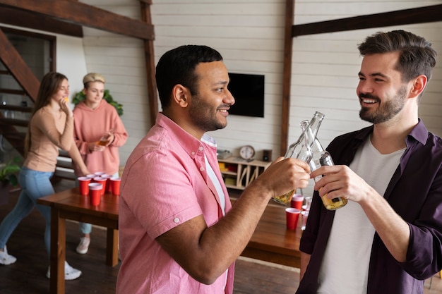 Gente vitoreando y bebiendo cerveza mientras juegan al beer pong en una fiesta interior