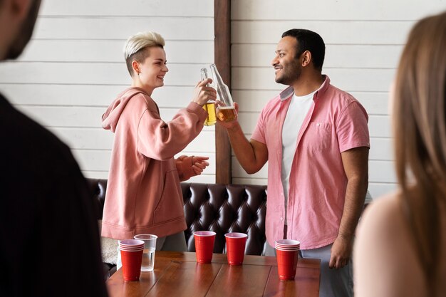 Gente vitoreando y bebiendo cerveza mientras juegan al beer pong en una fiesta interior