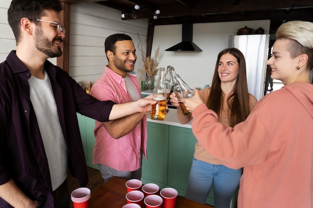 Gente vitoreando y bebiendo cerveza mientras juegan al beer pong en una fiesta interior