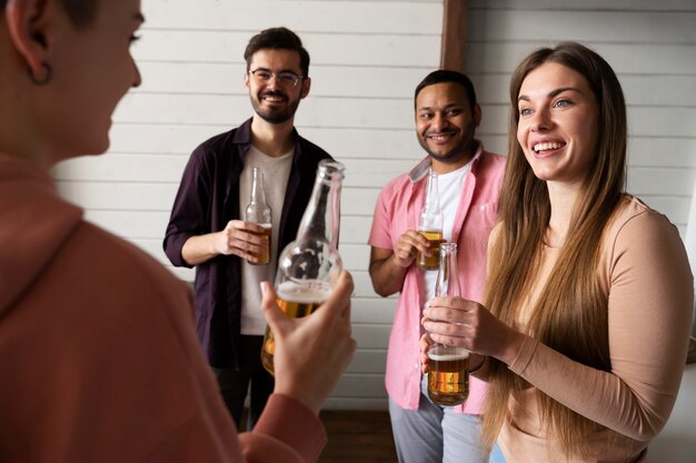 Gente vitoreando y bebiendo cerveza mientras juegan al beer pong en una fiesta interior