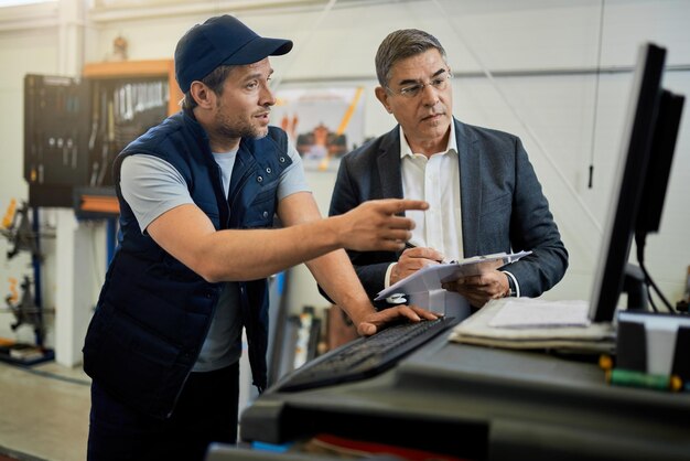 Gerente adulto medio y mecánico de automóviles hablando mientras usa una computadora en un taller de reparación de automóviles