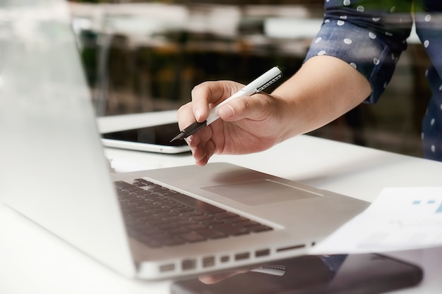 Gerente asiático de la mujer de negocios que analiza datum en cartas y que mecanografía en la computadora, haciendo notas en documentos en la mesa en la oficina, color de la vendimia, foco selectivo. Concepto de negocio.