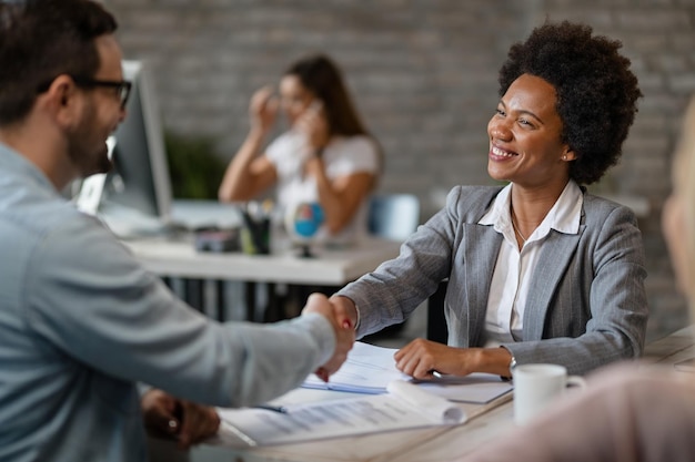 Gerente de banco afroamericano feliz estrechando la mano de un cliente después de un acuerdo exitoso en la oficina