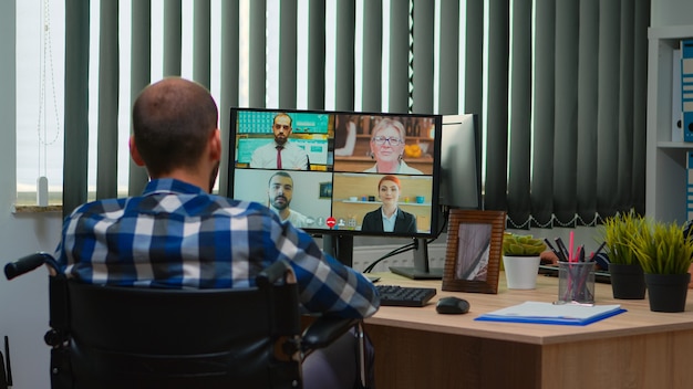 Gerente de discapacitados discapacitados en silla de ruedas hablando durante la videollamada con conferencia en línea en la oficina de negocios. Trabajador autónomo paralizado e inmovilizado que trabaja en una empresa financiera con tecnología moderna.