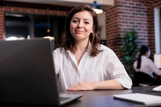 Gerente ejecutivo de una empresa de negocios positiva y amigable sentado dentro del espacio de la agencia. Mujer adulta joven caucásica sentada en el espacio de trabajo de la oficina mientras sonríe sinceramente a la cámara.