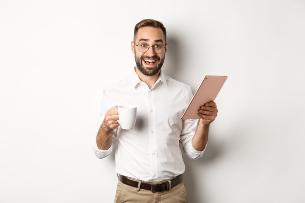 Gerente emocionado leyendo en tableta digital, trabajando y tomando café, de pie