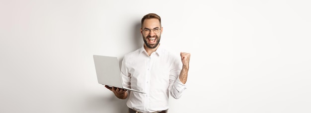 Foto gratuita gerente feliz de negocios ganando regocijo en línea con bomba de puño sosteniendo una computadora portátil y suplente triunfante