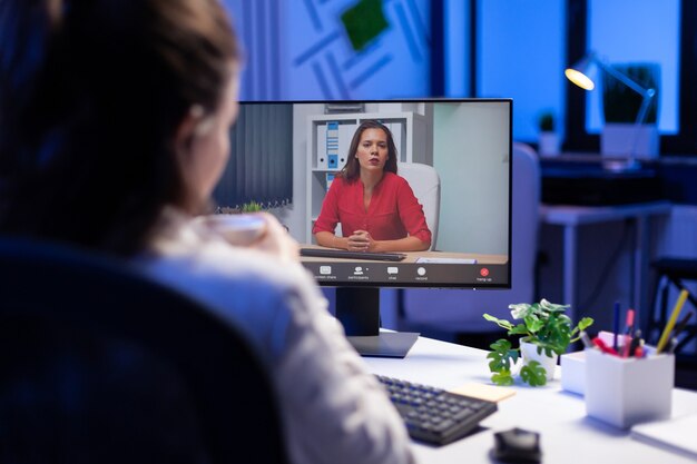 Gerente hablando con compañeros de equipo durante la teleconferencia en línea a la medianoche desde la estrategia de marketing de planificación de la oficina de negocios