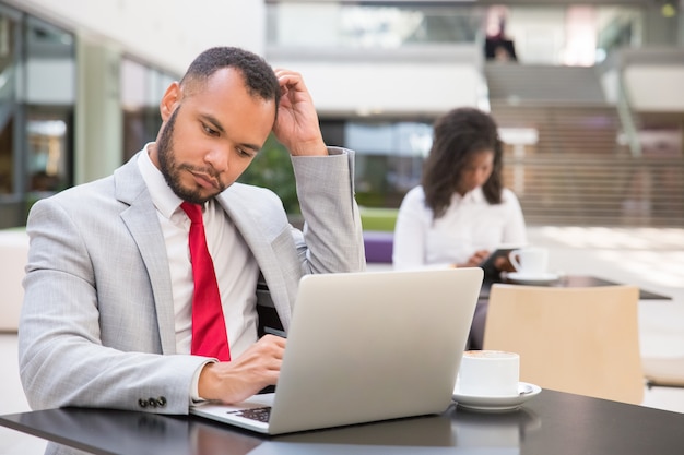 Gerente hombre pensativo usando laptop mientras bebe café