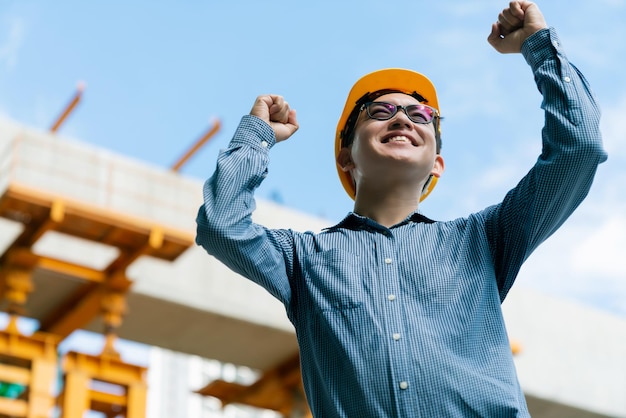 Foto gratuita gerente de ingeniero asiático inteligente entregado con éxito con uniforme de seguridad que verifica la construcción del sitio con antecedentes de estructura de acero y hormigón