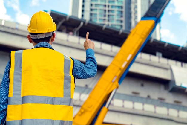 Gerente de ingeniero asiático inteligente con uniforme de seguridad que verifica la construcción del sitio con antecedentes de estructura de acero y hormigón