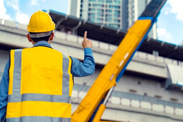 Gerente de ingeniero asiático inteligente con uniforme de seguridad que verifica la construcción del sitio con antecedentes de estructura de acero y hormigón