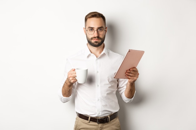 Gerente masculino confiado leyendo trabajo en tableta digital y tomando café, de pie