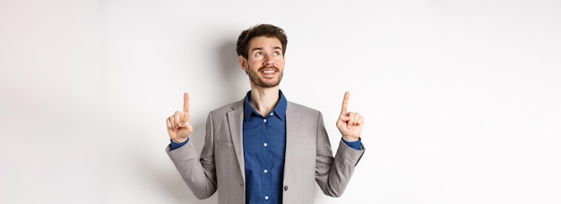 Foto gratuita gerente masculino sonriente de ensueño en traje señalando y mirando cara feliz mirando publicidad st
