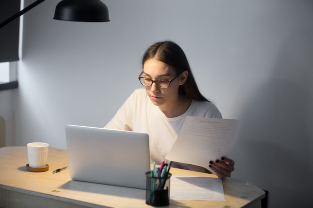 Foto gratuita gerente del milenio en gafas trabajando en una computadora portátil y sosteniendo un documento