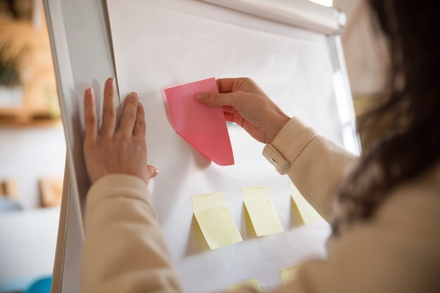 Gerente de mujer pegando notas de papel en blanco en el rotafolio