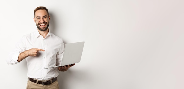 Foto gratuita gerente de negocios guapo en gafas trabajando en una computadora portátil apuntando a la computadora y sonriendo complacido stan