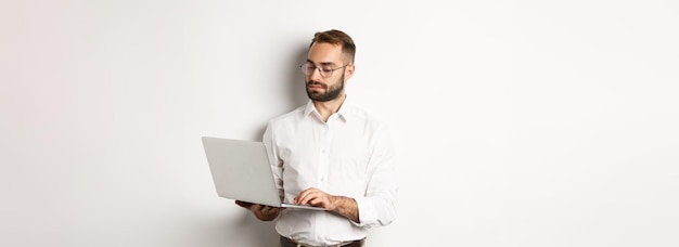 Foto gratuita gerente serio de negocios que trabaja en una computadora portátil de pie sobre fondo blanco