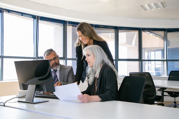 Los gerentes de la empresa discutiendo las ganancias y analizando el informe. Empresarios sentados en la mesa de reuniones, mirando el monitor de la computadora, sosteniendo papel. Concepto de comunicación empresarial o trabajo en equipo