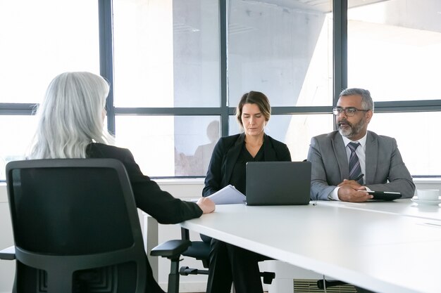 Gerentes de empresa serios hablando con candidato de trabajo en la entrevista. Vista posterior, copie el espacio. Concepto de empleo y carrera