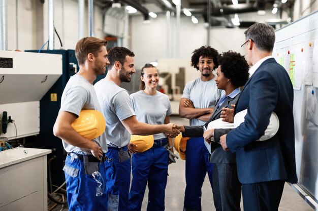 Los gerentes de la empresa visitan a sus empleados en una fábrica. Una mujer de negocios afroamericana feliz le da la mano a un trabajador.