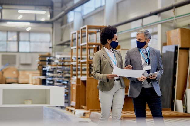 Gerentes de empresas con mascarillas protectoras hablando mientras caminan por las instalaciones de la fábrica de madera