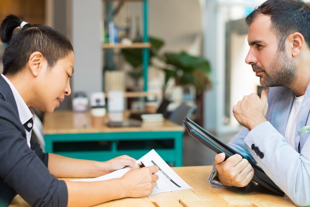 Gerentes latinos y asiáticos sentados y trabajando con documentos en oficina.