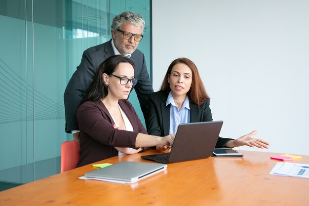 Los gerentes que muestran la presentación en la computadora portátil al ejecutivo, señalando la pantalla, explicando los detalles.