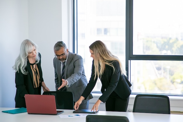 Gerentes que muestran la presentación del proyecto al jefe. Hombre de negocios apuntando con la mano a la pantalla del portátil y hablando con sus colegas. Plano general. Concepto de comunicación empresarial