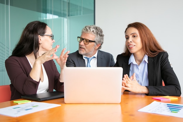 Gerentes reunidos en una mesa con una computadora portátil abierta, discutiendo y compartiendo ideas con el jefe.