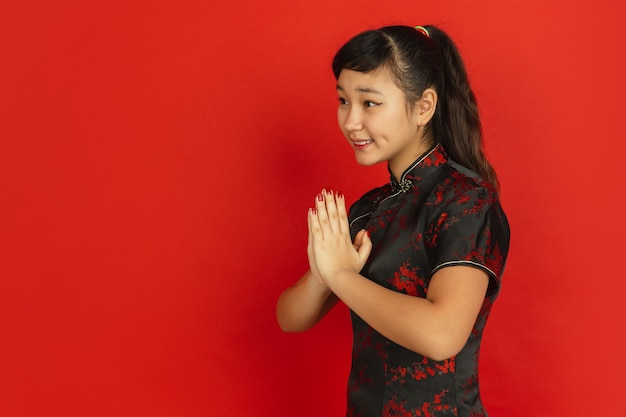 Gesticular, gracias al lado. Feliz año nuevo chino 2020. Retrato de joven asiática sobre fondo rojo. Modelo femenino en ropa tradicional se ve feliz. Celebración, emociones humanas. Copyspace.