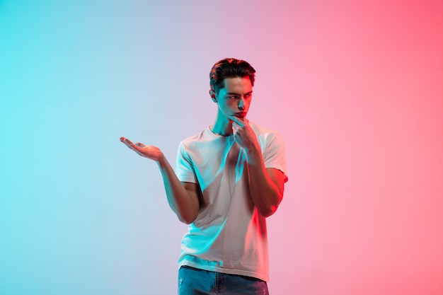 Gesticular. Retrato de joven hombre caucásico en estudio degradado azul-rosa en luz de neón