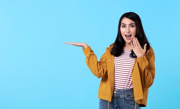 Gesto asiático joven de la mujer que presenta una idea con la mano abierta para copiar el espacio aislado en fondo azul.