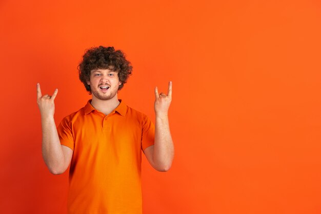 Gesto de cuerno de roca. Retrato monocromático del hombre joven caucásico en estudio anaranjado.