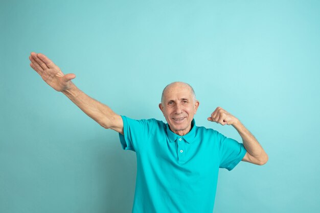 Gesto de éxito ganador. Retrato de hombre mayor caucásico sobre fondo azul de estudio. Hermoso modelo emocional masculino. Concepto de emociones humanas, expresión facial, ventas, bienestar, publicidad. Copyspace.