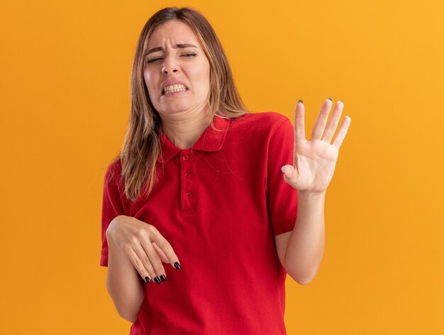 Gestos de mujer bonita joven descontento dejar de signo de mano aislado en la pared naranja