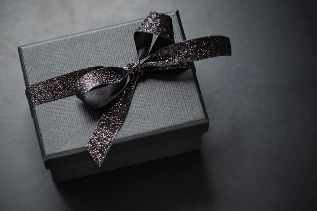 Giftbox negro oscuro con cinta negra sobre fondo oscuro. De cerca