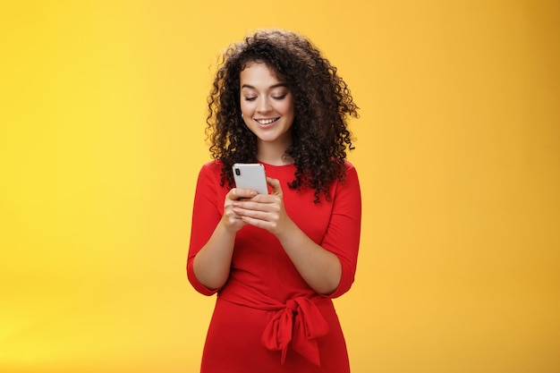 Gil enviando un mensaje difundió noticias a través de la red social que invitó a amigos a una fiesta a través de un teléfono inteligente sosteniendo el teléfono móvil en las manos sonriendo ampliamente en la pantalla del dispositivo como posando sobre fondo amarillo.