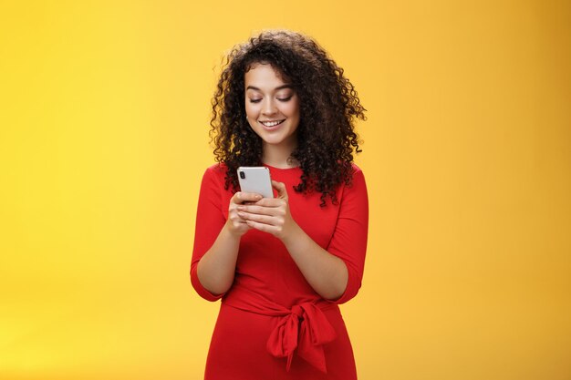 Gil enviando un mensaje difundió noticias a través de la red social que invitó a amigos a una fiesta a través de un teléfono inteligente sosteniendo el teléfono móvil en las manos sonriendo ampliamente en la pantalla del dispositivo como posando sobre fondo amarillo.