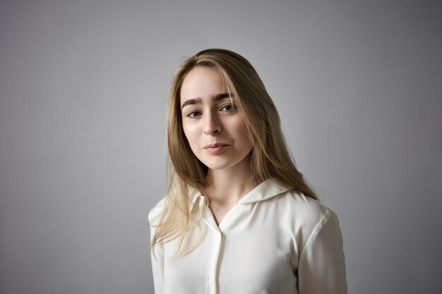 Gilr bonita con estilo con pecas y cabello rubio suelto mirando a la cámara con alegre expresión facial feliz. Atractiva mujer joven de belleza natural posando aislada en la pared de estudio de espacio de copia en blanco